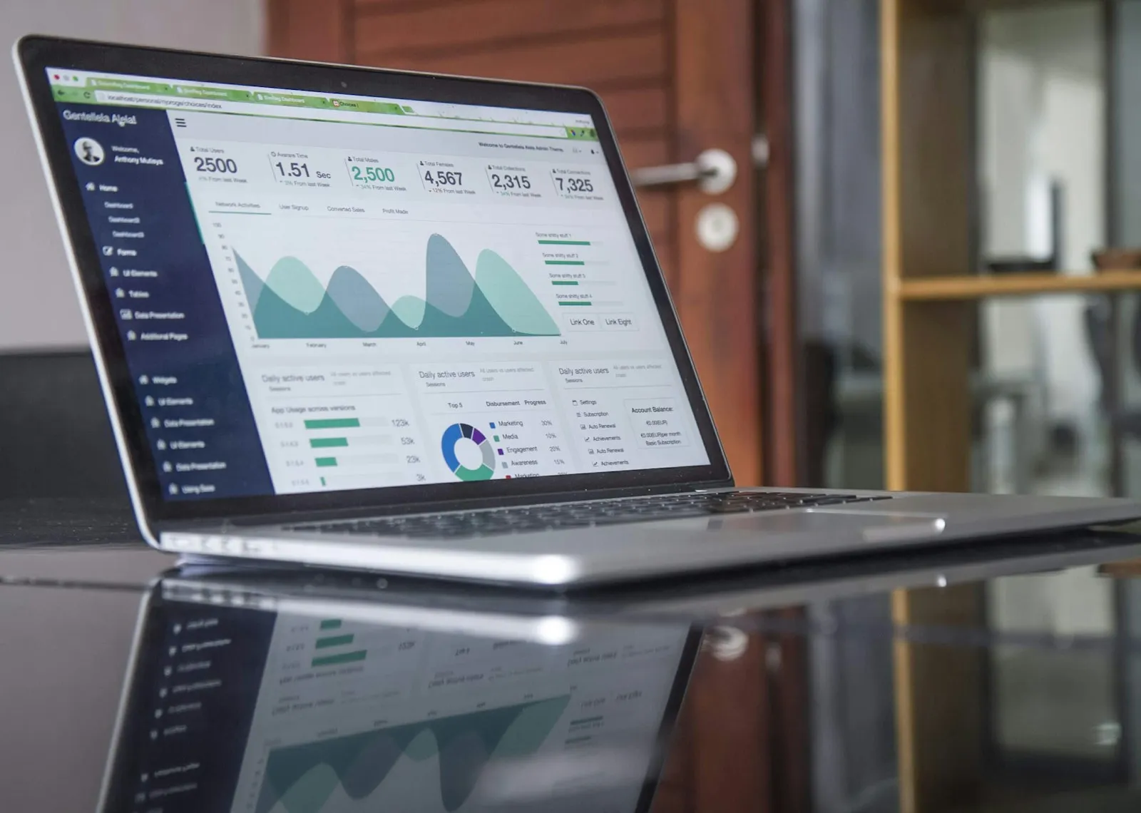 A laptop on a glass-top table displaying analytics graphs, the kind of view you use to check email campaign performance after sending.