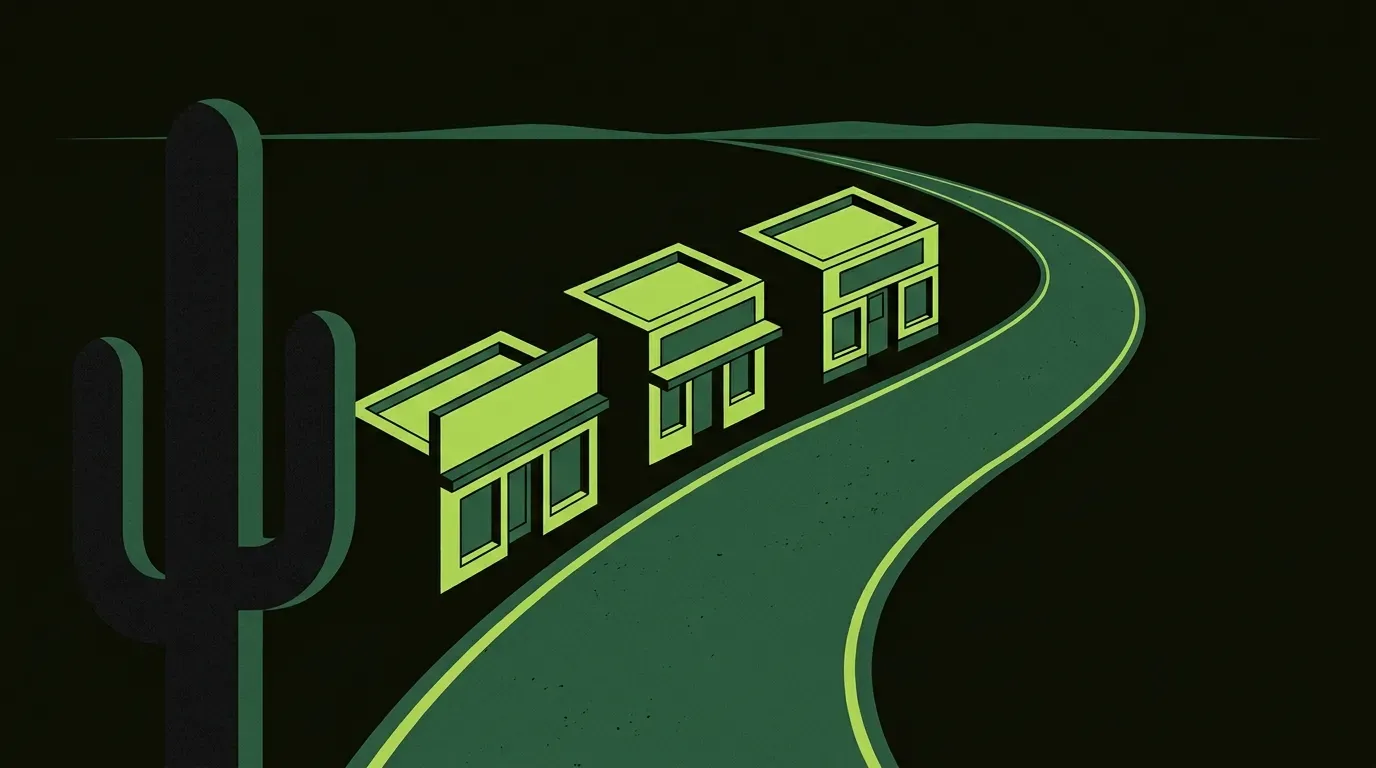 An isometric western main street scene at dusk along a dusty desert road, three small storefronts with clean geometric facades, a prominent saguaro silhouette on one side.