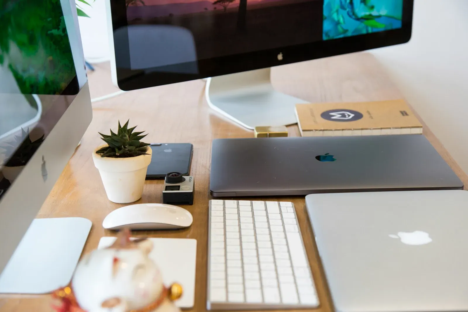 A clean wooden desk topped with a computer monitor, keyboard, and a small plant — a designer’s workspace in natural daylight.