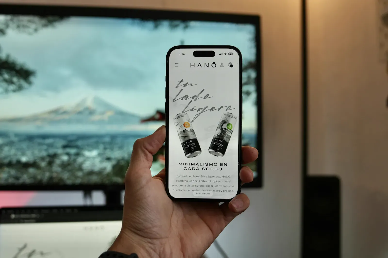 A hand holding a smartphone displaying a small-business website, with drinks on the table behind it.