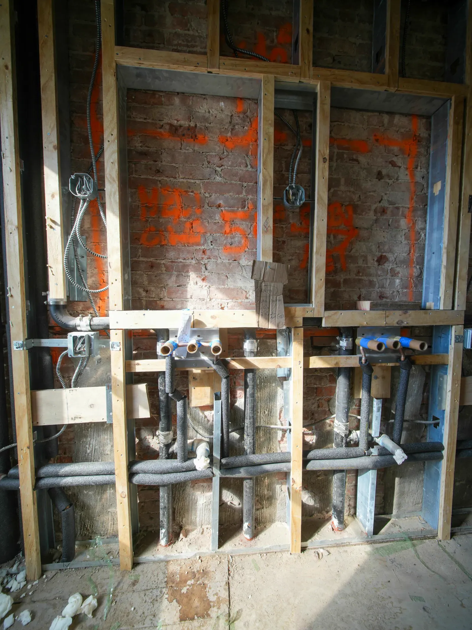 Plumbing and electrical work in progress inside an open wall, showing a tradesperson’s skilled hands-on labor.