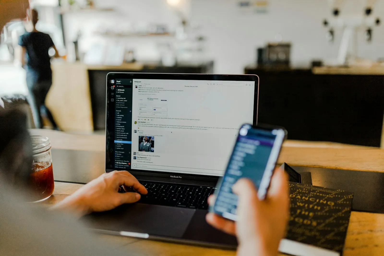 A person using a smartphone alongside a laptop on a workspace, the typical multi-device setup for managing an email marketing program.