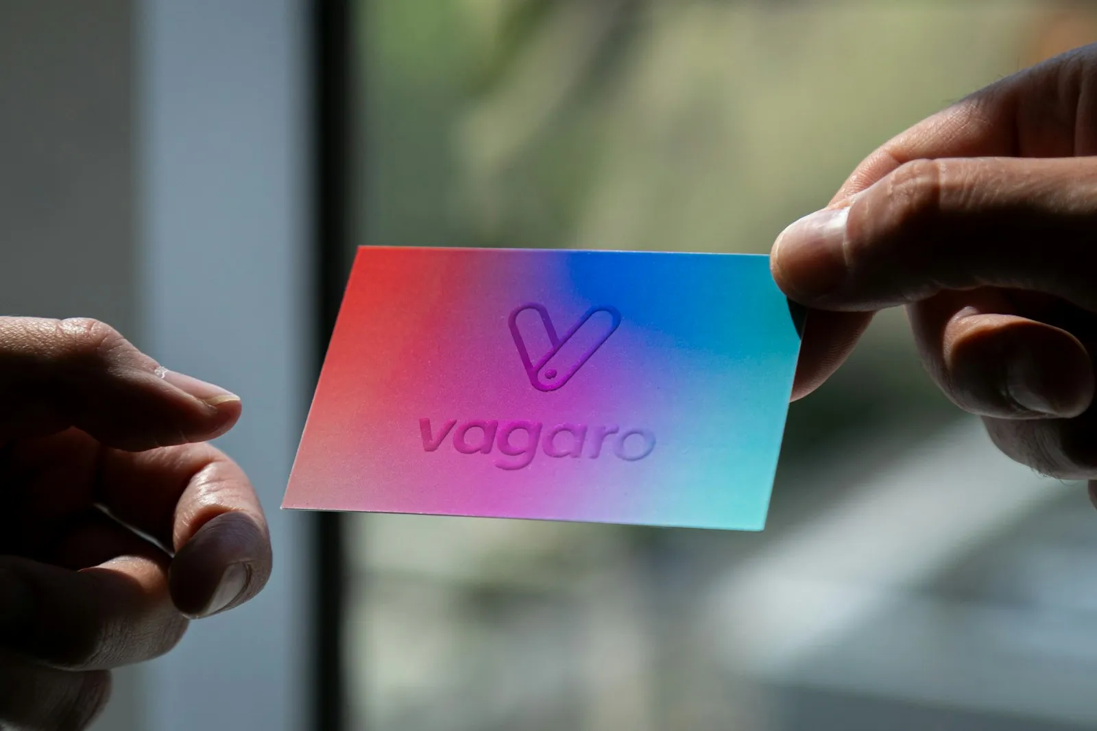 Hands holding a colorful printed brand card, representing the physical surface where a brand identity actually lands in front of a customer.