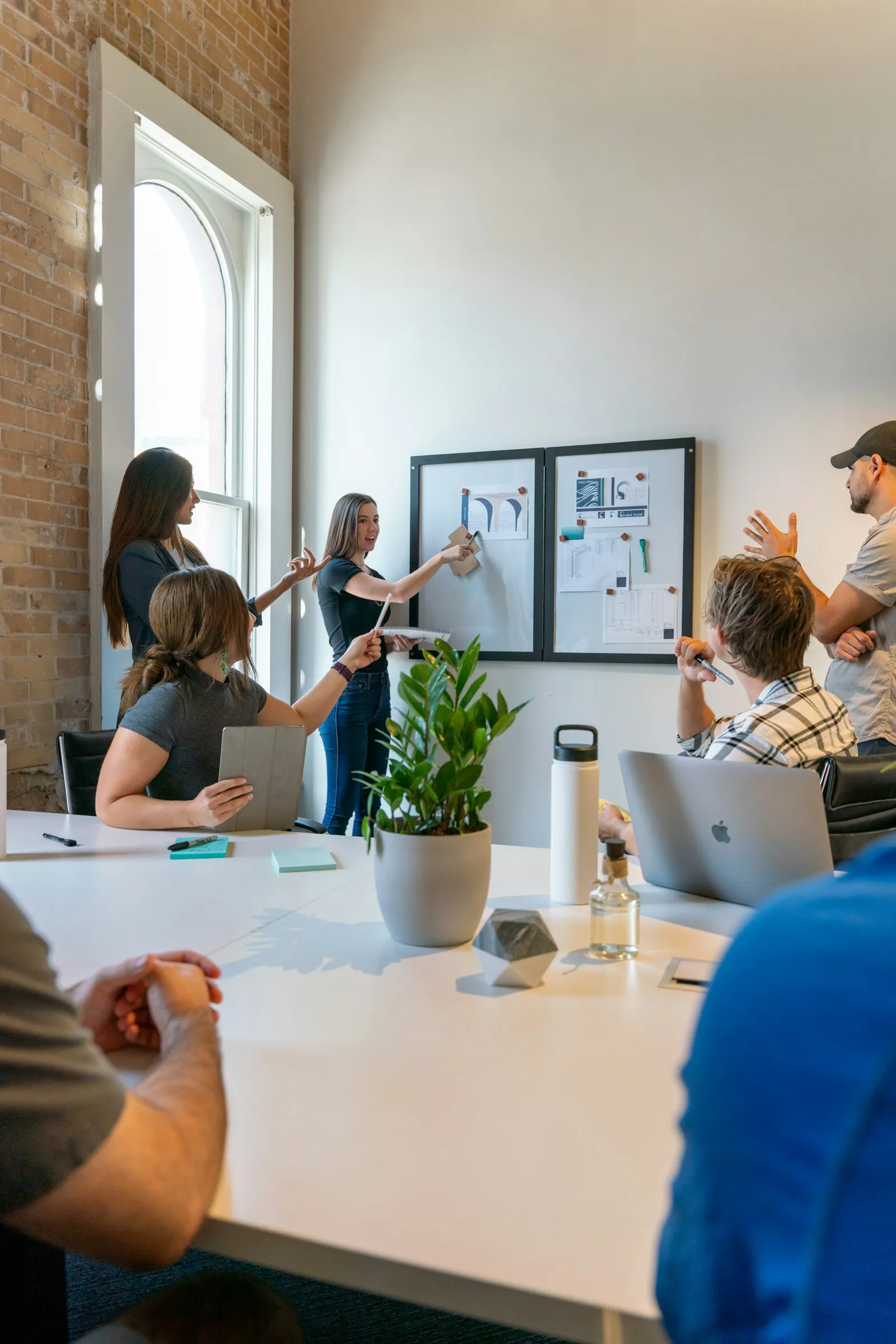 A small group of people gathered around a white table in a workspace, the typical scene of a small in-house marketing team coordinating with the owner.