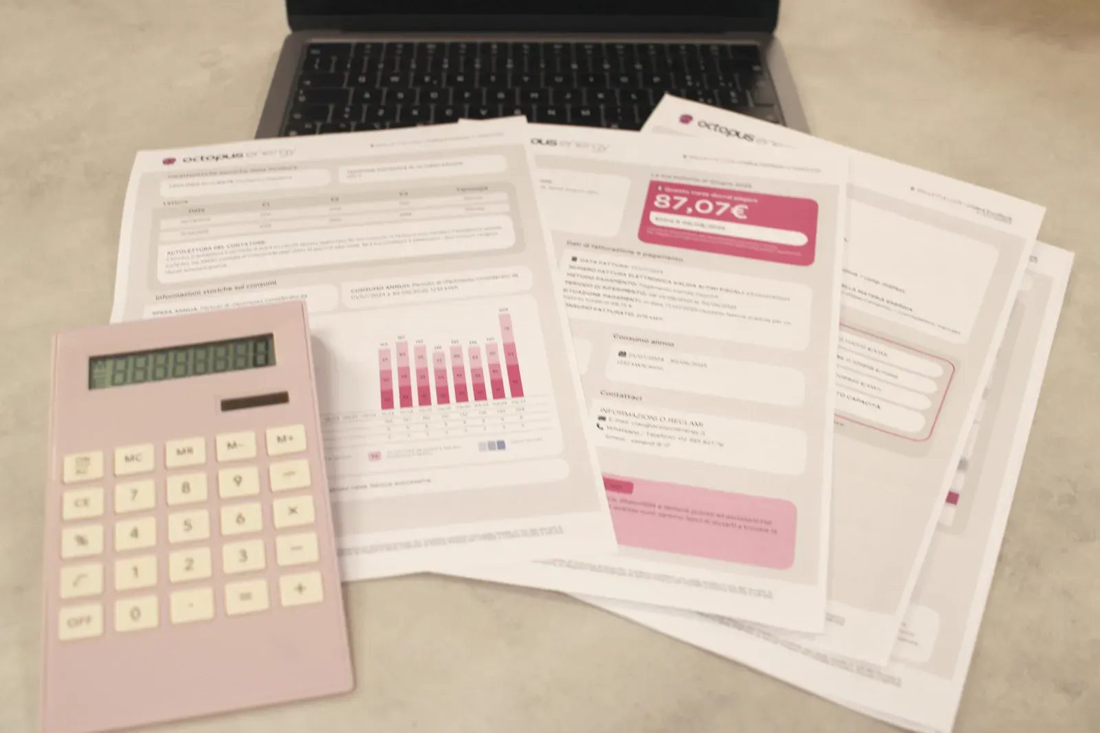A small business owner reviewing bills, with a calculator and a laptop showing financial figures on the desk.