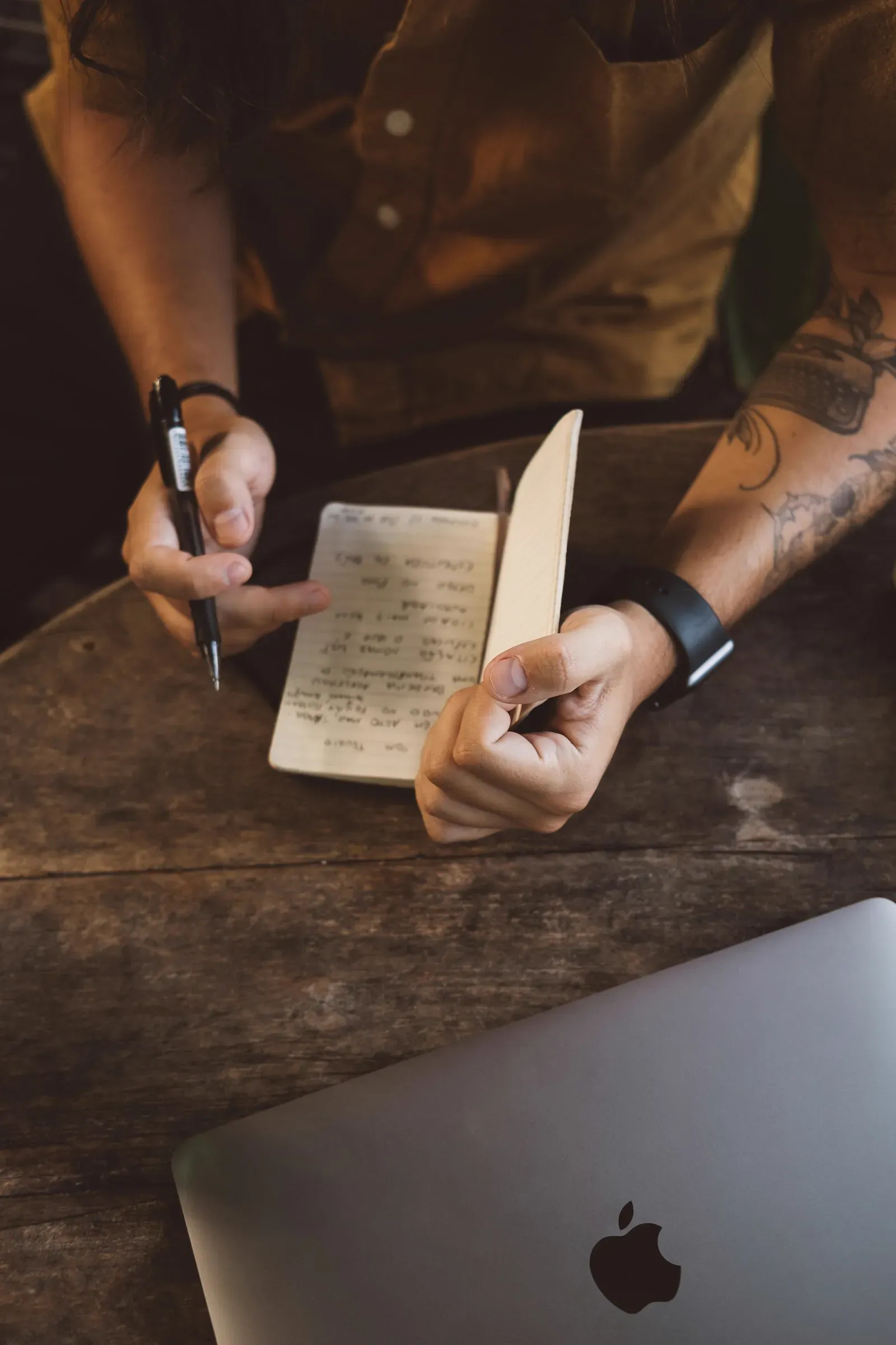 A person sitting at a wooden table writing in a notebook, planning during a focused work session.
