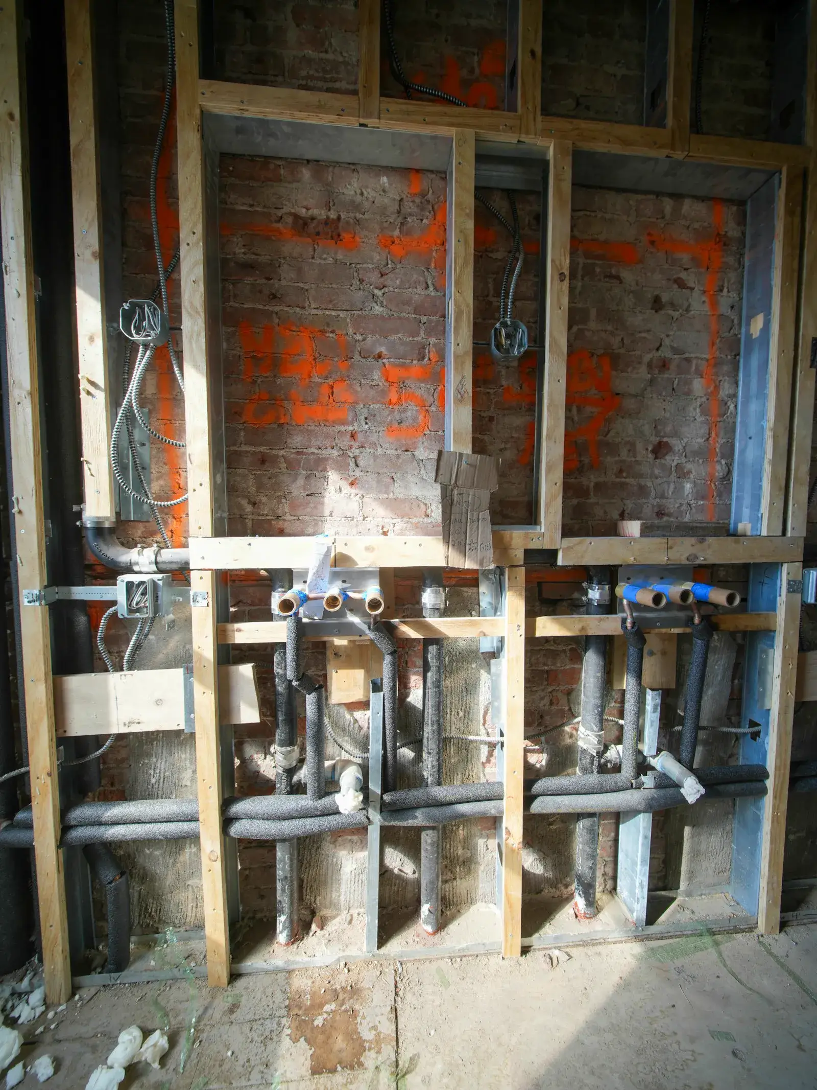 Plumbing and electrical work in progress inside an open wall, showing a tradesperson's skilled hands-on labor.