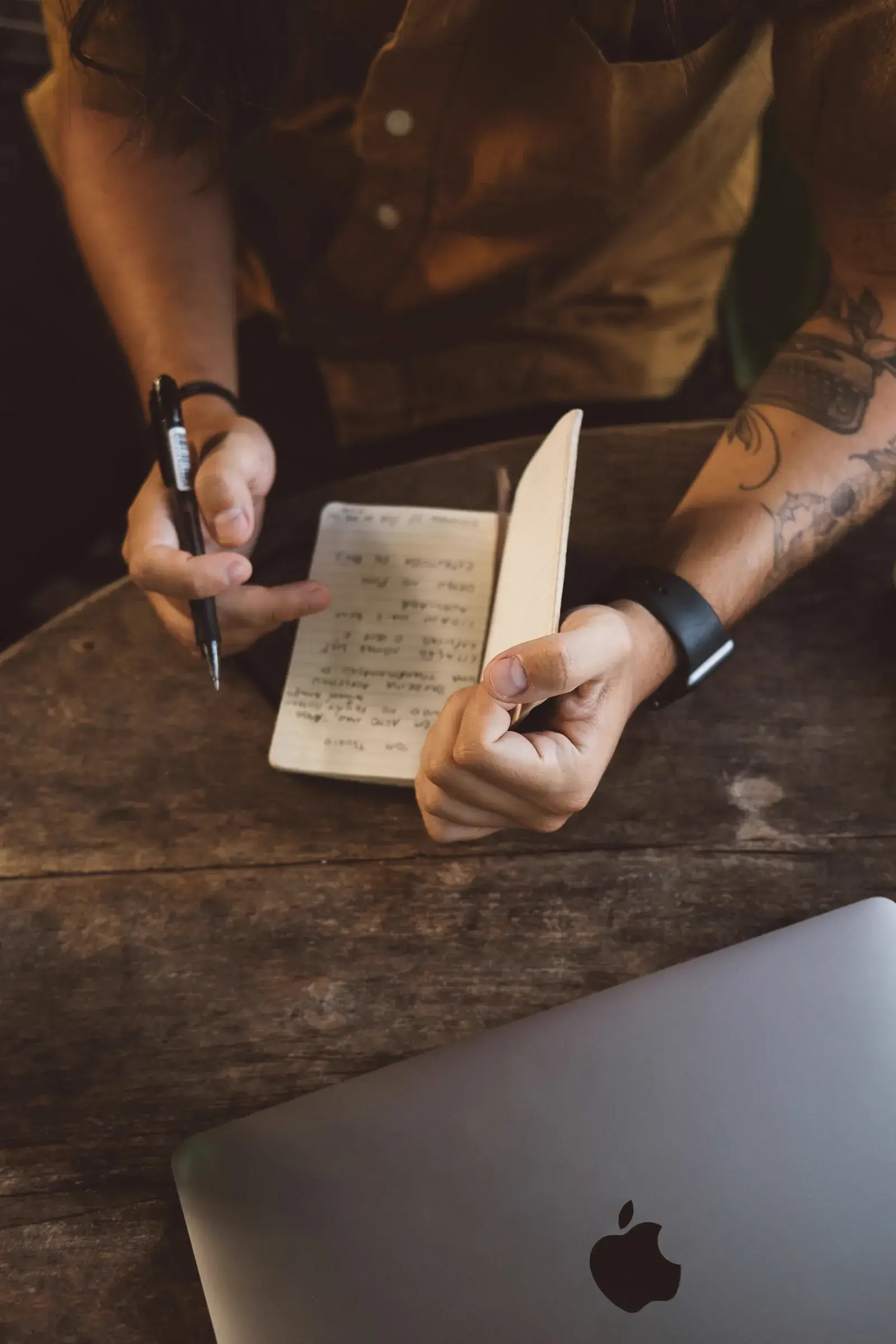 A person sitting at a wooden table writing in a notebook, planning during a focused work session.